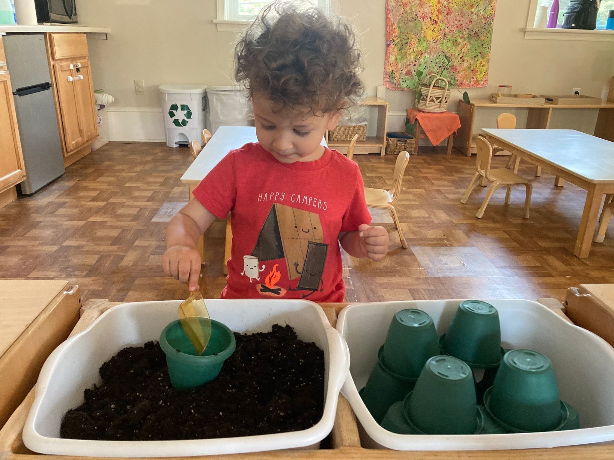 A toddler focused on scooping sand onto the pot during the work period. This activity refines the motor skills and improves the child's hand- eye coordination.