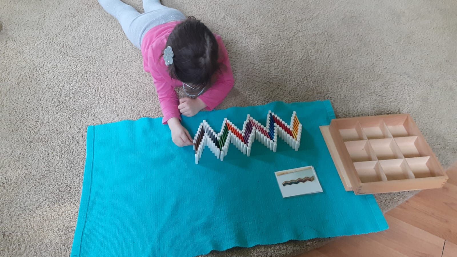 A child busy working with color box; grading the color tablets from darkest to lightest while making a specific pattern after referring to the control card.
